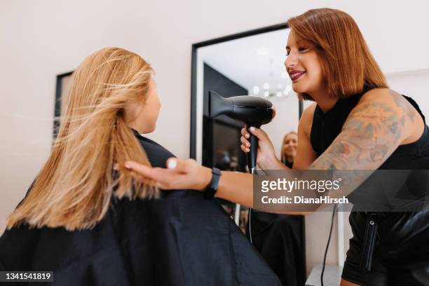 beautiful female hairdresser dries a blonde woman's hair with a hair dryer in the hair salon - beauty salon stock pictures, royalty-free photos & images