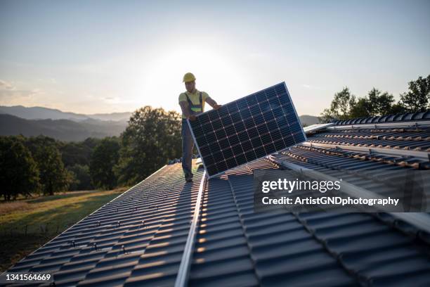workers placing solar panels on a roof - zonnepanelen stockfoto's en -beelden