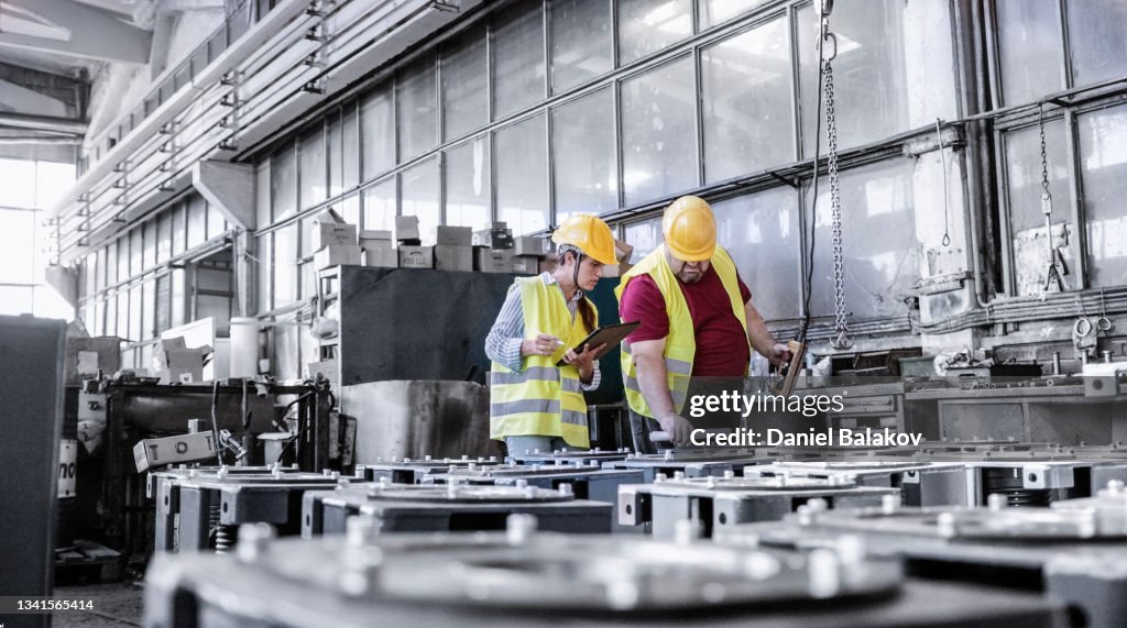 Engineers working in metal manufacturing industry, doing quality control of the production with tablet.