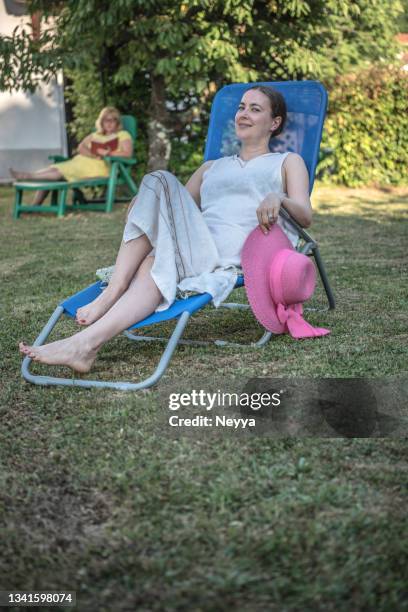 woman sitting in deck chair, relaxing in the garden on summer afternoon - deckchair funny stock pictures, royalty-free photos & images