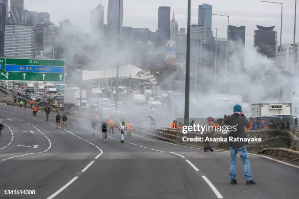 Smoke is seen as along the Westgate bridge as Protestors blocked the road as thousands march through Melbourne after State Government announces...