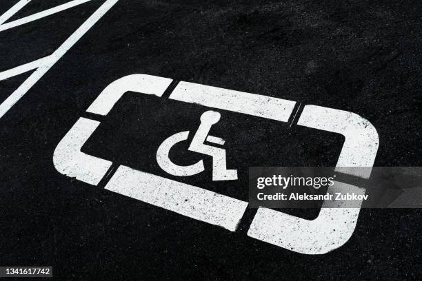 a wheelchair symbol painted on the gray asphalt in the parking lot. a sign of a parking space for visitors with disabilities. free parking with free space for cars of disabled people. traffic sign, road markings. - acceso para sillas de ruedas fotografías e imágenes de stock