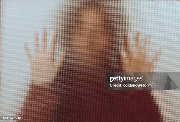 domestic abuse victim with hands pressed against glass window - escape stockfoto's en -beelden