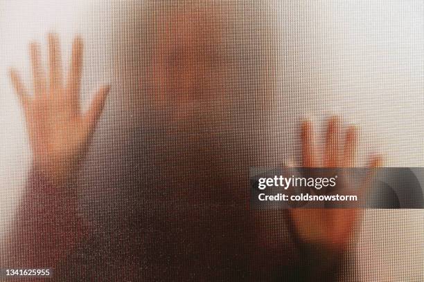 domestic abuse victim with hands pressed against glass window - human trafficking stockfoto's en -beelden