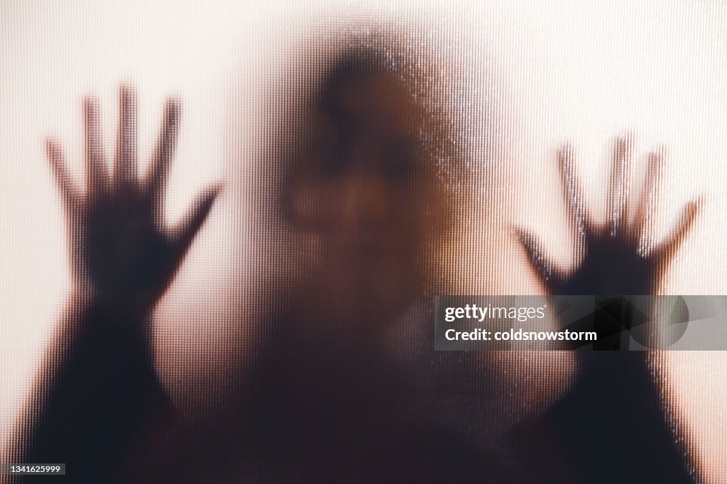 Domestic abuse victim with hands pressed against glass window