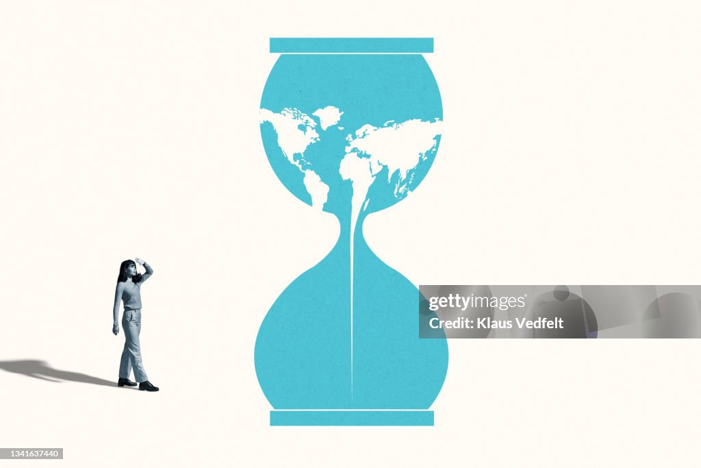 Woman shielding eyes by blue hourglass with world map