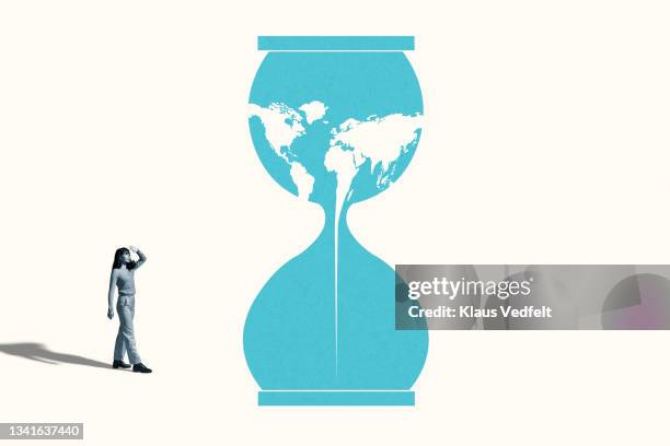 woman shielding eyes by blue hourglass with world map - time blocking stock pictures, royalty-free photos & images