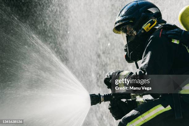 faceless firemen in safety helmets and protective uniform extinguishing fire with water hose during training on sunny day - feuerwehrmann stock-fotos und bilder