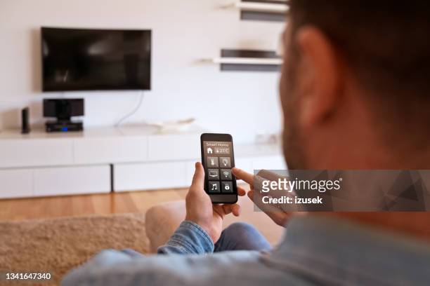 man controlling smart devices using phonet at home - telephone switch stock pictures, royalty-free photos & images
