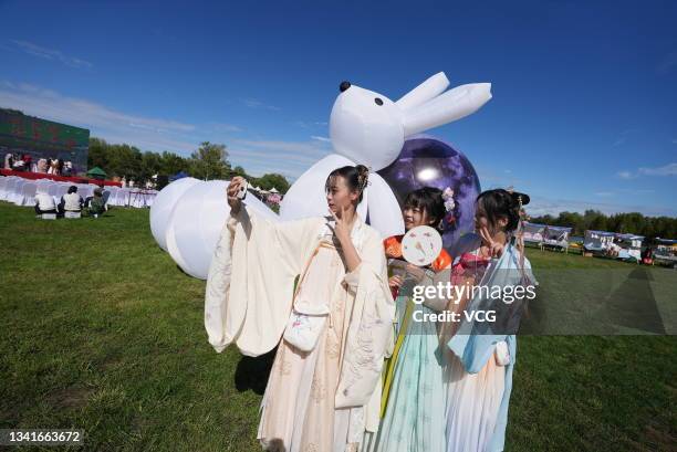 Tourists wearing traditional Han costumes take a selfie in front of art installations of the moon and rabbit at Flower Port during the Mid-Autumn...
