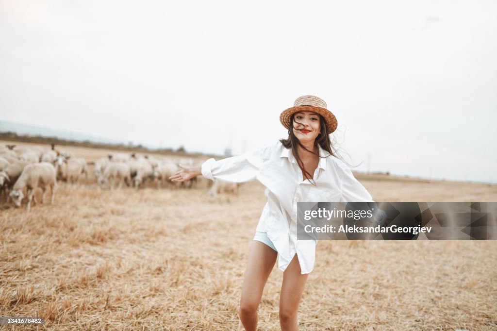 Bellezza femminile eccitata che corre di fronte alle pecore sui campi di fieno