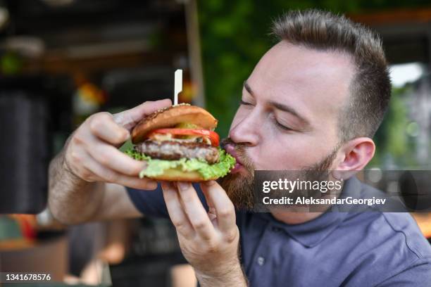 maschio affamato che mangia delizioso hamburger - adults eating hamburgers foto e immagini stock