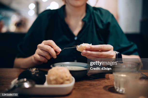 close up, mid-section of young asian woman applying butter on fresh bread while having lunch in restaurant. eating out lifestyle - untar de mantequilla fotografías e imágenes de stock