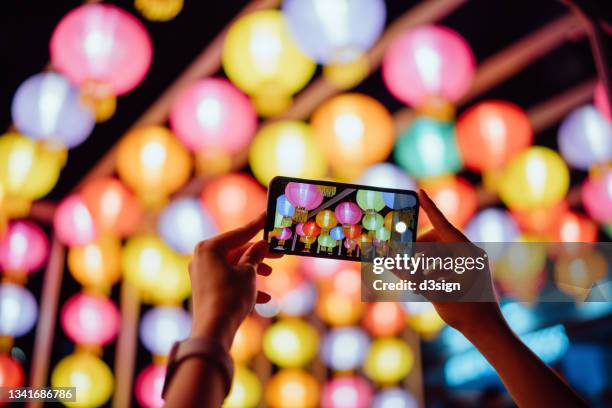 close up of woman's hands taking photos of illuminated and colourful traditional chinese lanterns with smartphone hanging on city street at night. traditional chinese culture, festival and celebration event theme - chinese lantern night stock pictures, royalty-free photos & images