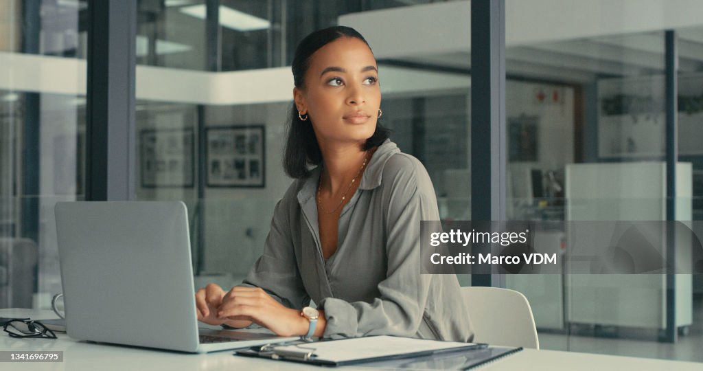 Shot of a beautiful young woman lost in thought while using her laptop in a modern office