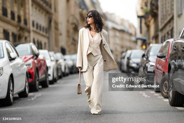 Fashion blogger Xiayan wears black sunglasses, a silver large chain necklace, a beige buttoned V-neck short sleeves jacket as a t-shirt, a matching...