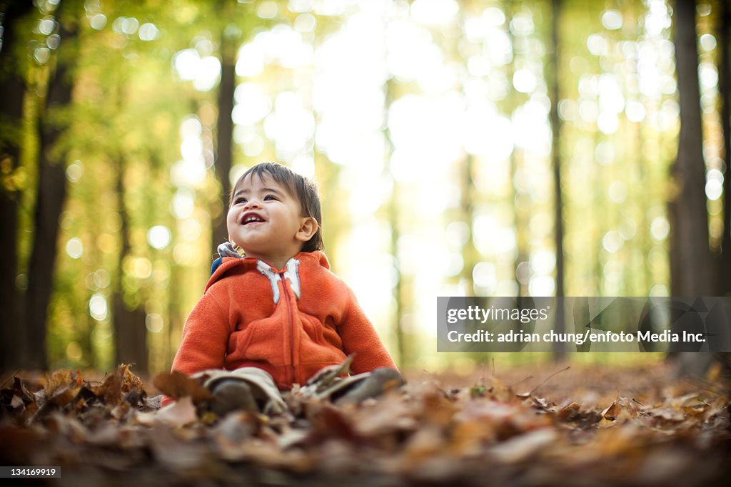 Little toddler plays with leaves in forest