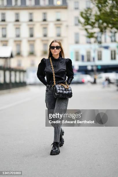 Julia Comil wears black cat eye sunglasses by Saint Laurent, a black silk blouse with puffed shoulders by Frame, a black shiny leather padded...