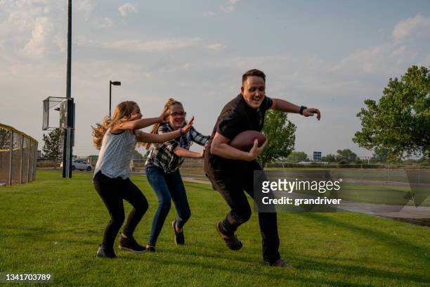 giovane padre che gioca a calcio touch con le sue due figlie su un campo erboso in un parco nel tardo pomeriggio estivo - afl ball foto e immagini stock