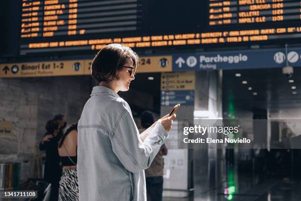 a young woman at a train station or airport looking at the arrival and departure boards - holiday travel ahead of thanksgiving clogs airports highways and train stations stockfoto's en -beelden