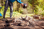 Man extinguishing campfire with water from cauldron in summer forest. Put out campfire. Traveling fire safety rules
