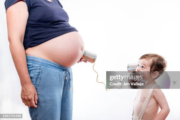 foto de perfil de un niño pequeño mirando a su madre mientras escucha la tripa de ella con un telefono hecho con latas y una cuerda. fondo blanco. - niño fondo blanco stock pictures, royalty-free photos & images