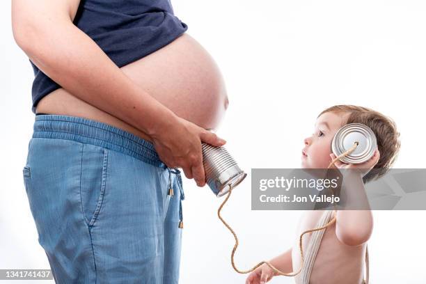 chico escuchando el abdomen de la madre embarazada con el teléfono de lata. fondo blanco - teléfono stock pictures, royalty-free photos & images