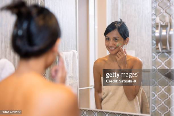 femme asiatique appliquant une crème pour la peau sur la joue dans la salle de bain - 薄ピンク photos et images de collection
