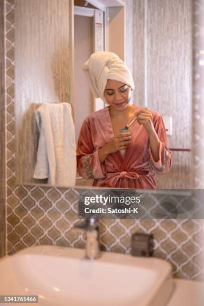 asian woman applying skin cream on cheek in bathroom - 薄ピンク stockfoto's en -beelden