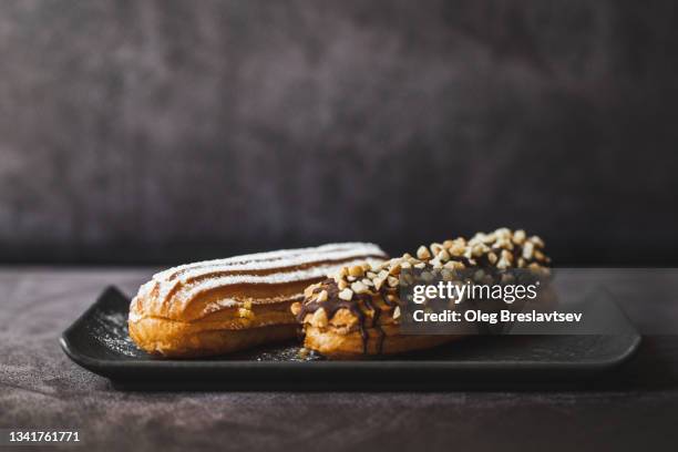 two tasty and delicious eclairs on black plate closeup. dark background - eclair stockfoto's en -beelden