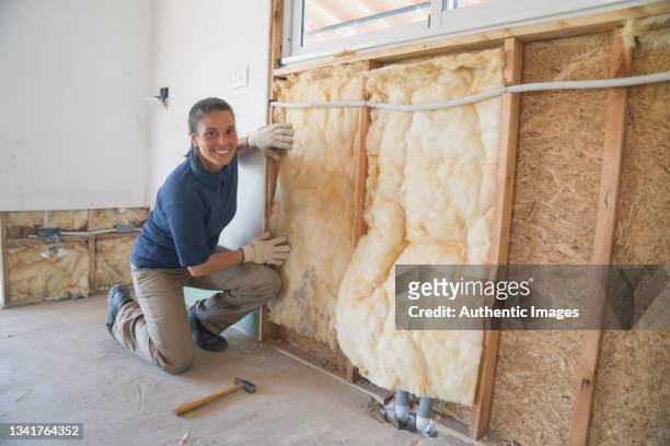 portrait of a female worker installing fiberglass insulation on wall during wood frame house construction - isolatiemateriaal stockfoto's en -beelden