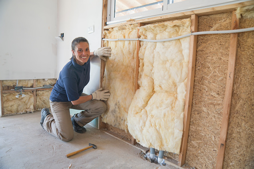 Portrait of a female worker installing fiberglass insulation on wall during wood frame house construction