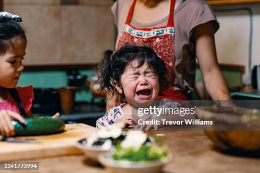 Mother preparing lunch with two young daughters as the younger one is crying Mother preparing lunch with two young daughters as the younger one is crying