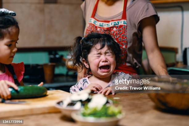 mother preparing lunch with two young daughters as the younger one is crying - tantrum stock pictures, royalty-free photos & images