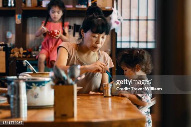 mid adult mother feeding her young daughter - japanese mom stock-fotos und bilder