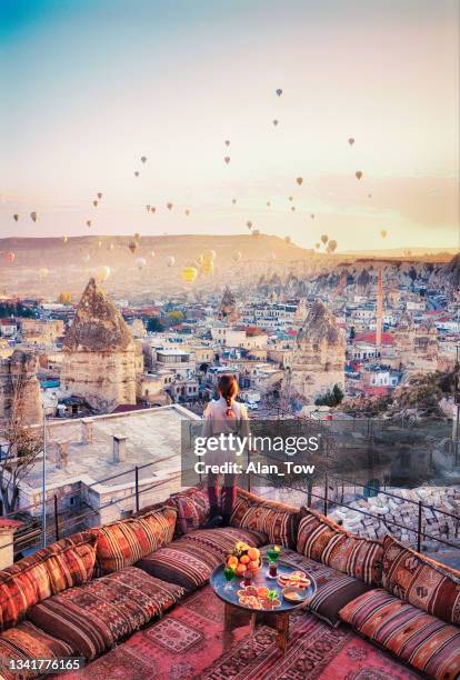 beautiful women stand at hotel rooftop watching hot air balloons flying over city ürgüp cappadocia, turkey - cappadocia stock pictures, royalty-free photos & images