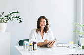 Young smiling brunette woman doctor nutritionist plus size in white shirt working at laptop at modern bright office room. The doctor prescribes a prescription for medicines and vitamins at clinic