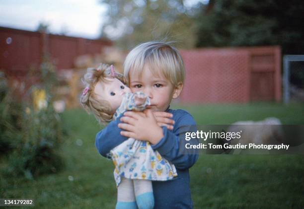 blonde infant boy hugging sisters doll - un solo niño bebé fotografías e imágenes de stock