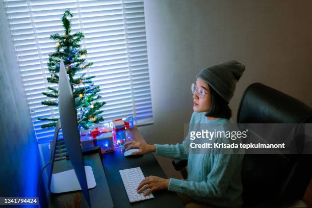 asian woman using  computer in her living room decorated for christmas. - homeowners decorate their houses for christmas stockfoto's en -beelden