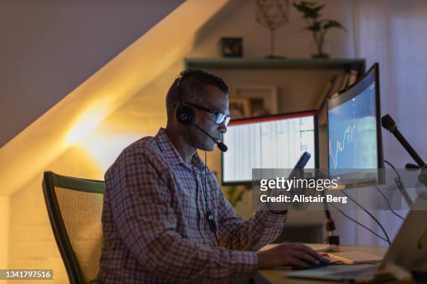 man looking at currency trading app on his smart phone from his home office - stock market traders stock pictures, royalty-free photos & images
