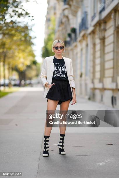 Emy Venturini wears black Prada sunglasses, gold large earrings, a black with a white slogan t-shirt from Kindom Shop, a white latte vintage blazer...