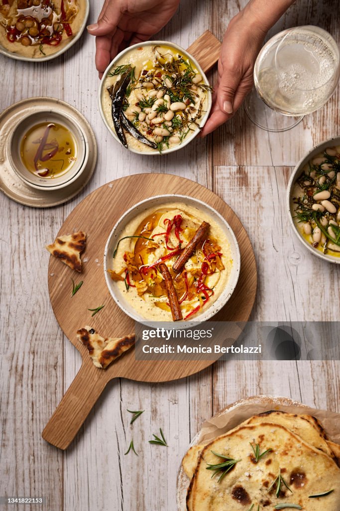 Hummus and cannellini beans dip with spices on wooden table with human hands holding bowl