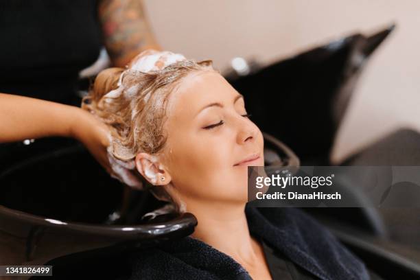 primo piano di una bella donna bionda che si gode con un sorriso il lavaggio dei capelli nel parrucchiere - head massage foto e immagini stock