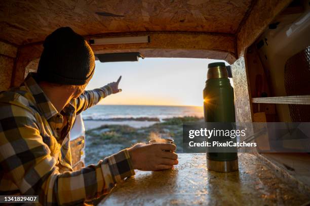 over shoulder view man points out to sea having hot drink in camper van - flask stock pictures, royalty-free photos & images