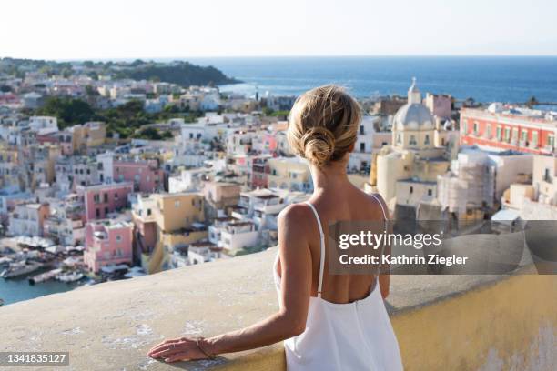 woman enjoying the view of the idyllic port of corricella, procida island, italy - woman summer dress stock-fotos und bilder