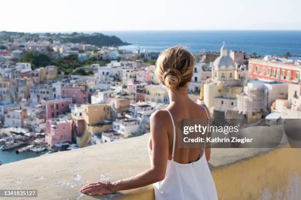 woman enjoying the view of the idyllic port of corricella, procida island, italy - femme robe blanche photos et images de collection