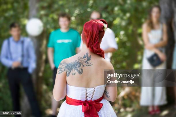 bride with a tattoo looking towards wedding guests outdoors - pin up wedding stock pictures, royalty-free photos & images
