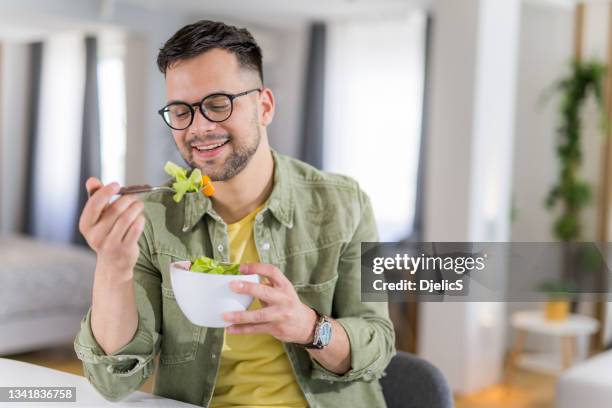 young man eating a salad at home. - eat man stock pictures, royalty-free photos & images