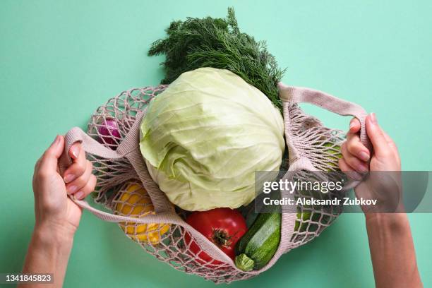 fresh ripe fruits or vegetables in a reusable shopping bag. a string bag made of recycled materials in the hands of a girl or woman, on a background or table. vegetarianism, veganism, raw food. cultivation of organic farm eco-products. no plastic and gmos - col fotografías e imágenes de stock