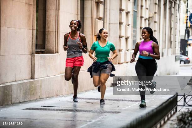 group of women running through urban area - running stock pictures, royalty-free photos & images